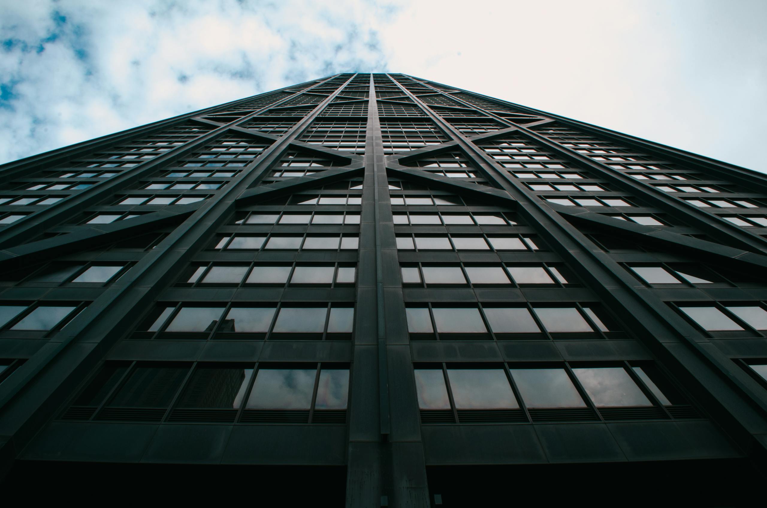 An upward perspective of a modern glass skyscraper against a cloudy sky in downtown Chicago.