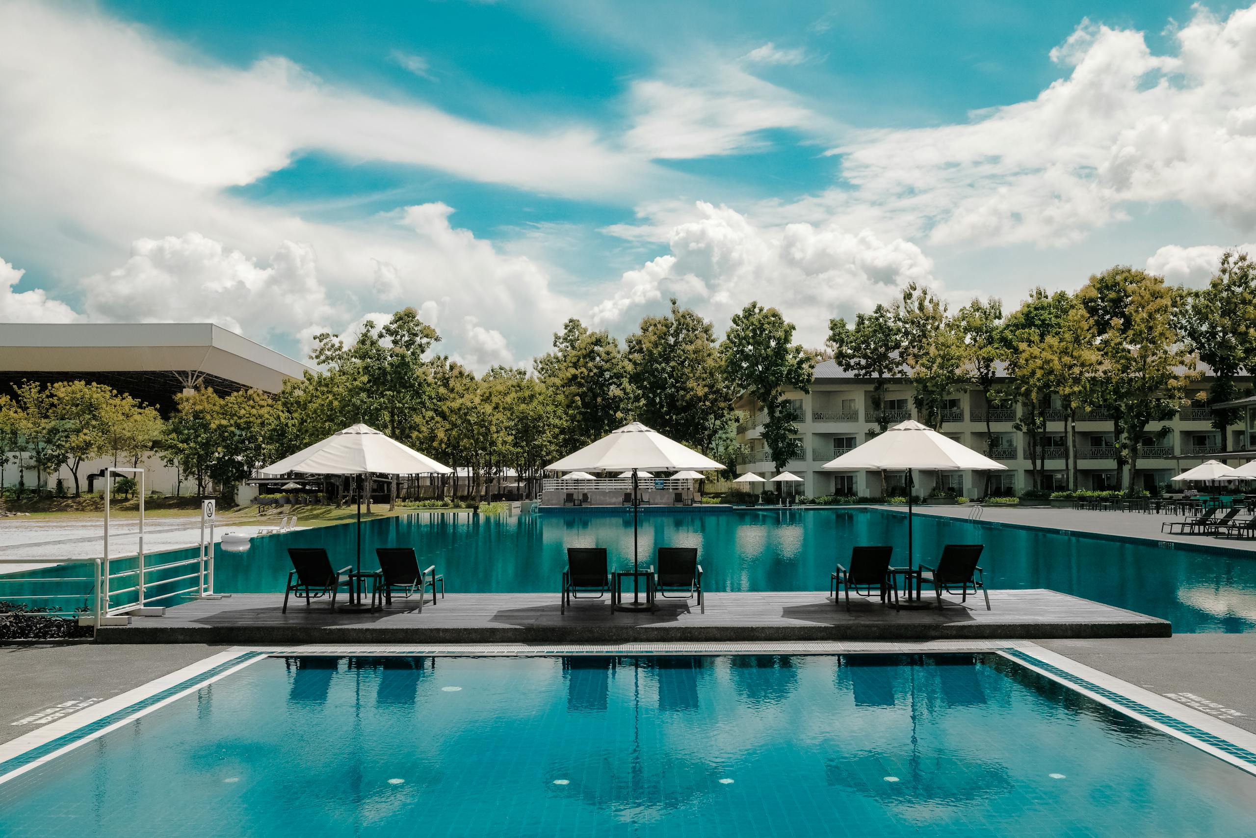 Explore a luxurious resort poolside with umbrellas and lounge chairs under a bright sky, perfect for summer vacations.