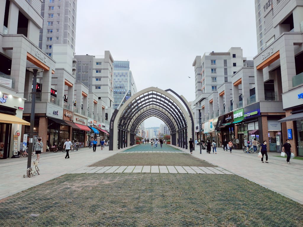 People walking through a modern shopping district in Hanam-si, South Korea, under a unique architectural arch.